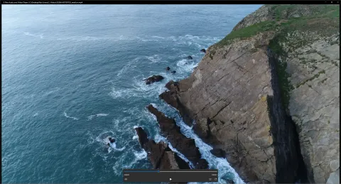 The video player showing an aerial view of sea cliffs, with a seek bar, play button and volume and window controls in a small panel at the bottom